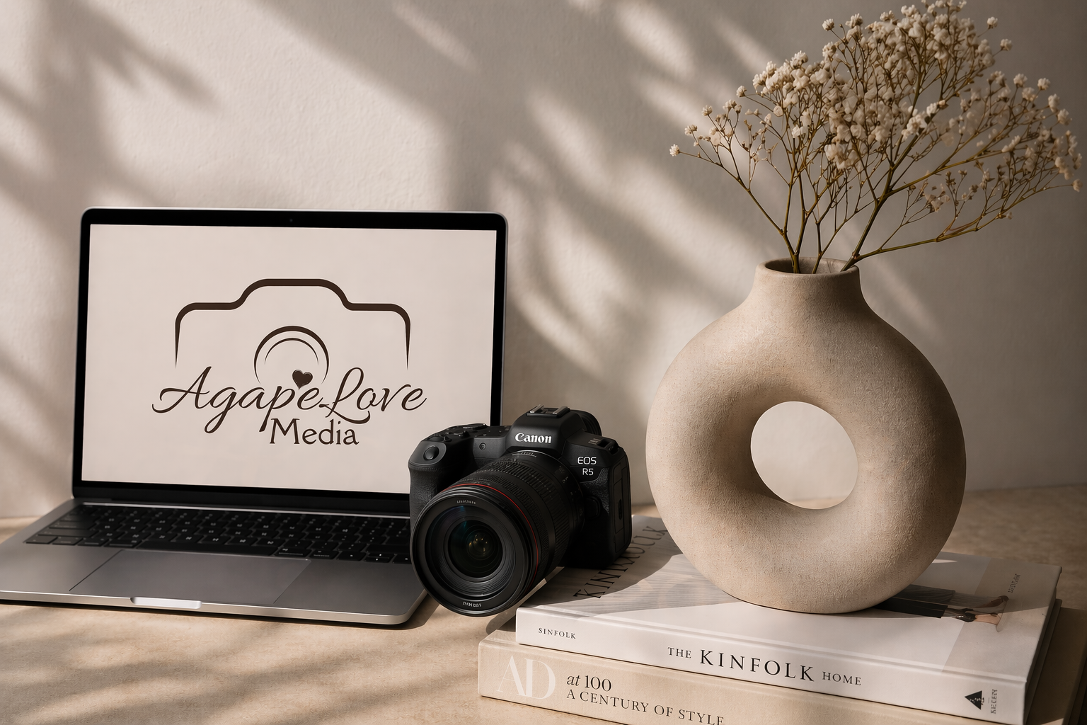 Laptop showing the Agapé Love Media logo beside a Canon camera and ceramic vase